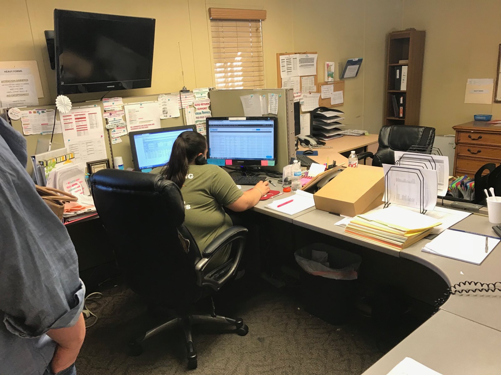 A salvage towing company's dispatch office: 2 dispatchers at desks with multiple monitors, papers pinned to the walls, boxes stacked on a desk.